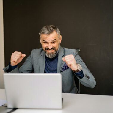 Happy businessman celebrating success while looking at laptop in modern office.