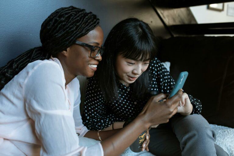 Two women relaxed on a sofa, sharing and enjoying moments on a smartphone.